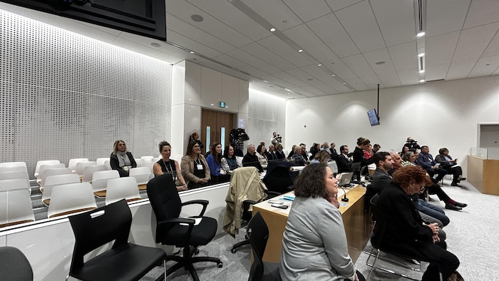 Plusieurs personnes sont assises dans une grande salle moderne munie de rangées de sièges blancs.