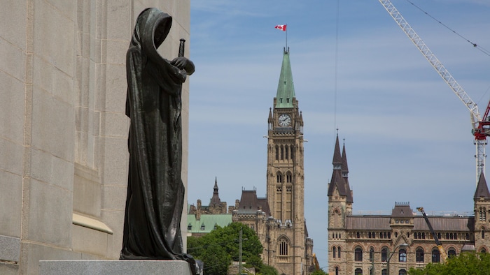 Au premier-plan, l'édifice de la Cour suprême avec une statue représentant la justice et, en arrière-plan, des édifices du Parlement canadien.
