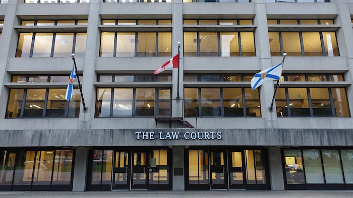 Trois drapeaux accrochés à des mâts devant l'entrée de l'édifice.