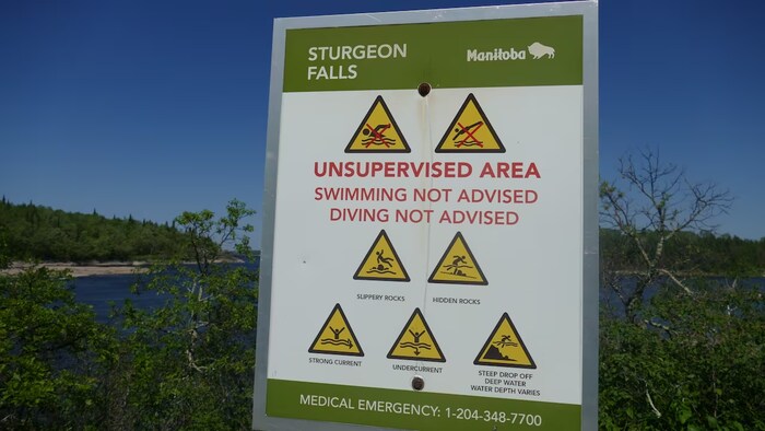 Un panneau indiquant aux gens de ne pas nager ou plonger dans un plan d'eau à proximité est affiché. Il signale également d'autres dangers, notamment les rochers glissants, les rochers cachés et les courants forts.
