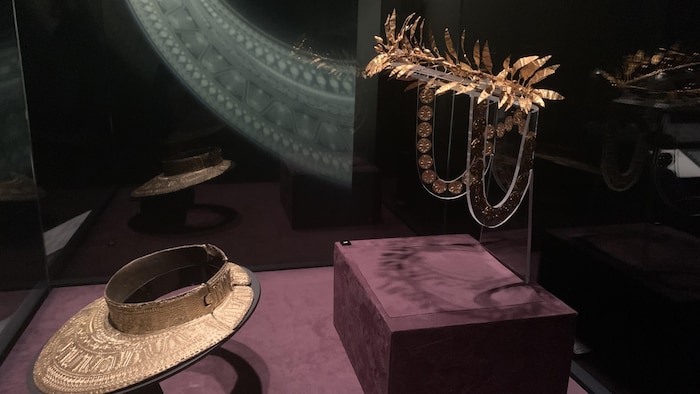 Une couronne et des objets précieux en or sont présentés derrière une vitrine dans un musée. 
