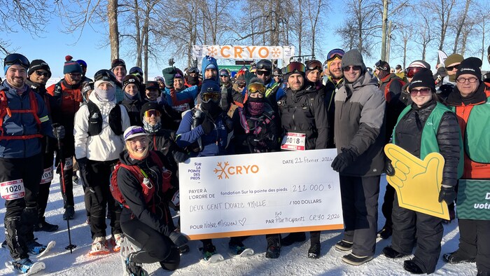Un groupe de participants en tenue d'hiver pose derrière un chèque géant de 212 000 $. Le chèque, daté du 21 février 2026, est destiné à la fondation « Sur la pointe des pieds » dans le cadre de l'événement CRYO.