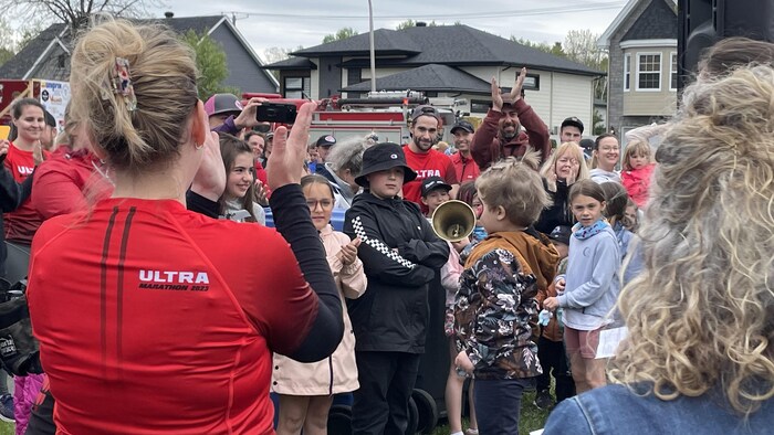 Des gens applaudissent une enfant qui secoue une cloche.