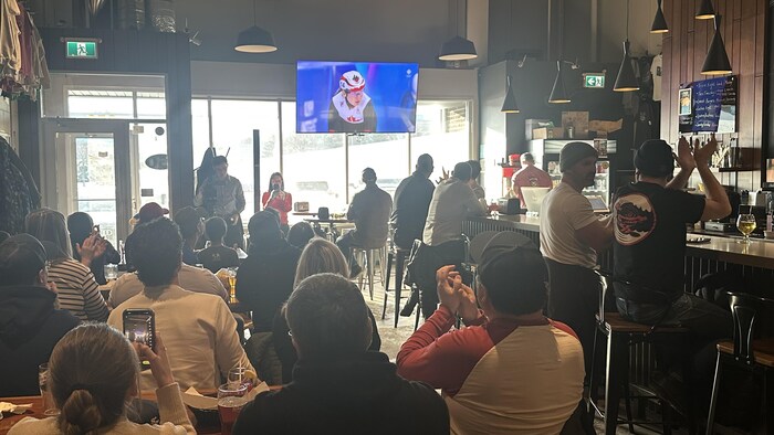 Des gens dans une brasserie regardent une épreuve des Jeux olympiques. 