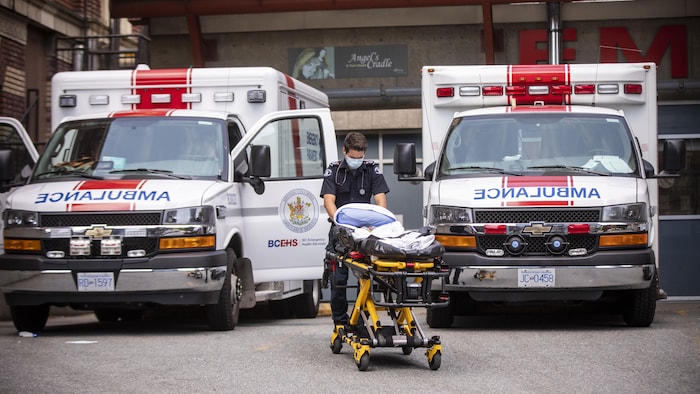 Un ambulancier pousse une civière entre deux ambulances à l'Hôpital St. Paul de Vancouver.