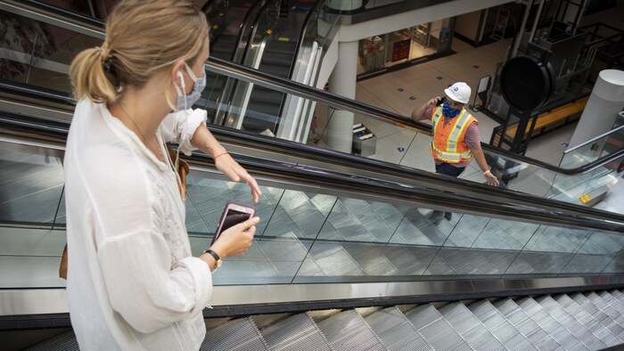 Une cliente et un ouvrier se croisent dans les escaliers roulants d'un centre commercial.