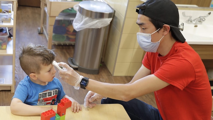 Un éducateur prend la température d'un enfant dans une garderie.