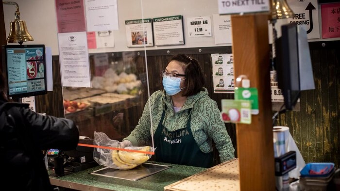 A woman wearing a face mask stands by a cash register in a store.