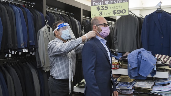 Un tailleur portant un masque mesure le cou d'un client portant lui aussi un masque.