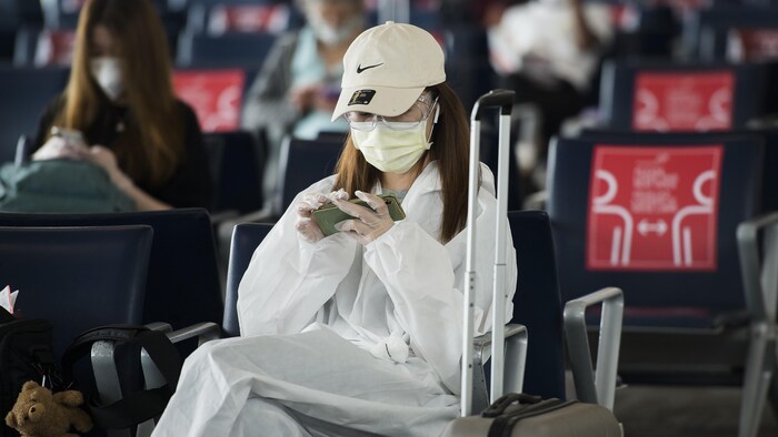 Des passagers assis portant un masque dans une aire d'attente pour l'embarquement à l'aéroport Pearson.