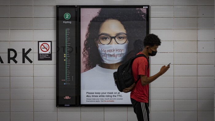 Un usager du métro portant un masque devant une affiche qui demande aux résidents de porter le masque dans les transports publics.