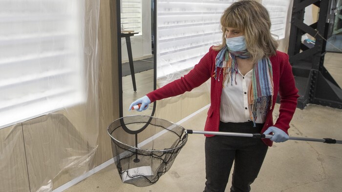 Une femme portant un masque de protection et des gants de caoutchouc désinfecte un filet à pêche dans une clinique d'optométrie.