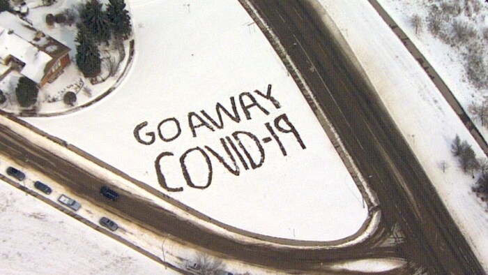 Une vue aérienne d'un message écrit en anglais dans la neige en bordure d'une route signifiant : « Vas-t-en, COVID-19! »