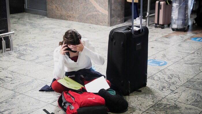 Une femme, assise par terre et entourée de ses bagages, parle au téléphone.
