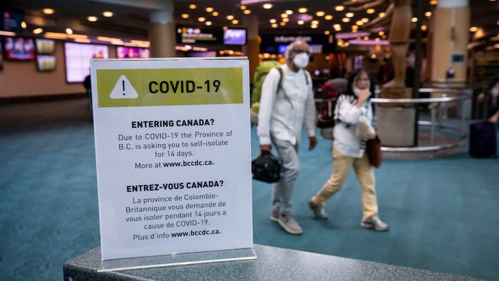 Deux passagers portant des masques marchent dans le hall d'entrée de l'Aéroport international de Vancouver au début de l'année 2020.