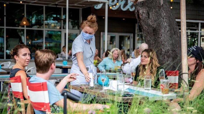 Une serveuse portant un masque sert des clients qui n'en portent pas.