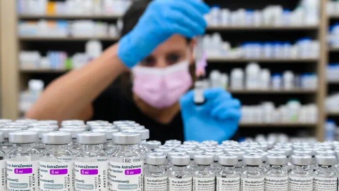 A pharmacist draws up a dose behind vials of both Pfizer-BioNTech and AstraZeneca-Oxford vaccines on the counter.