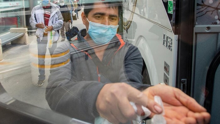 A man uses hand sanitizer as he boards a bus.