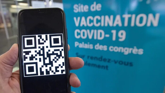 Une main tient un téléphone intelligent sur lequel est affiché un code QR.