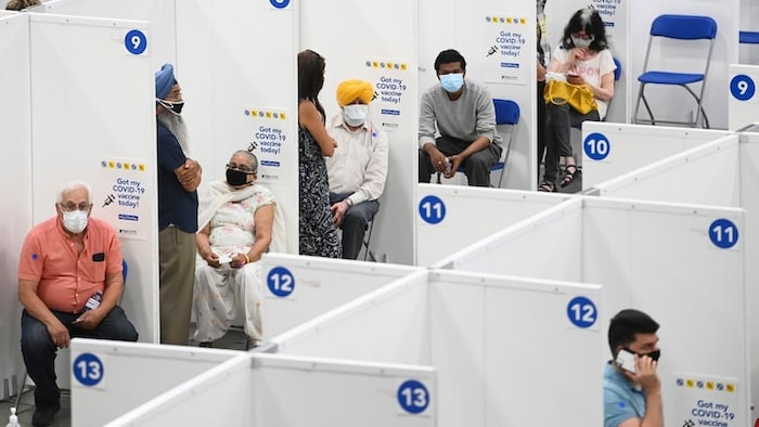 Des gens se font vacciner contre la COVID-19 en rang dans un aréna.