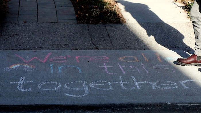 Un message solidaire en anglais est écrit sur le sol dans une rue de Toronto : « Nous sommes tous dans le même bateau ».