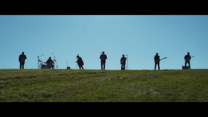 Sept artistes jouent de la musique sur une colline verdoyante. 