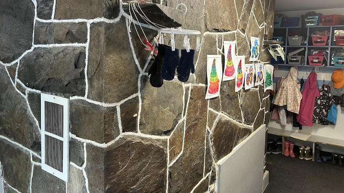 Un mur de pierres auquel sont accrochés des dessins d'enfants.