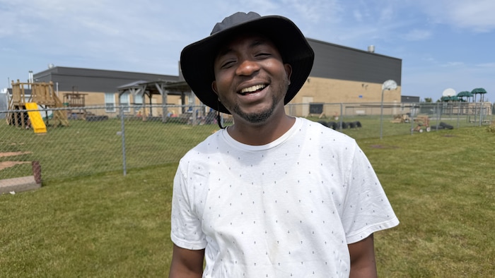 Un homme portant un chapeau mou pour se protéger du soleil est debout sur la pelouse en été et éclate de rire.
