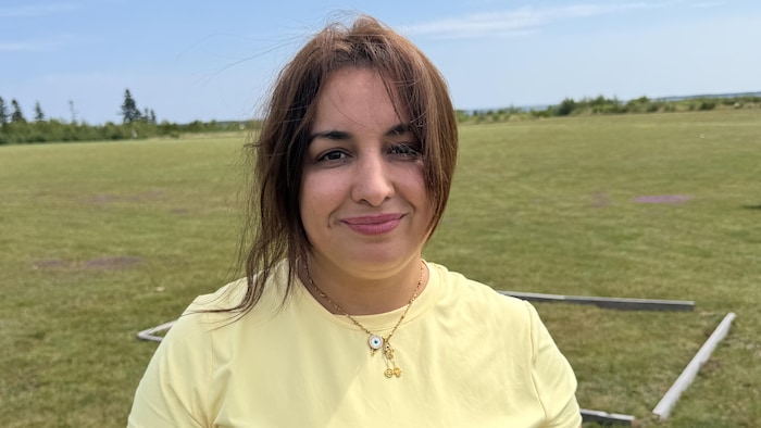 Une femme aux cheveux longs en chandail jaune debout sur la pelouse en été avec un beau ciel bleu à l'horizon.