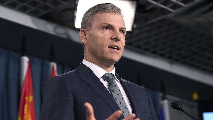 Plan moyen de Tim McMillan à un podium devant des drapeaux.