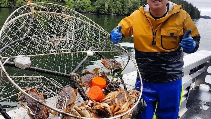 Un homme sur une barque est debout près d'un casier contenant plusieurs crabes dormeurs.