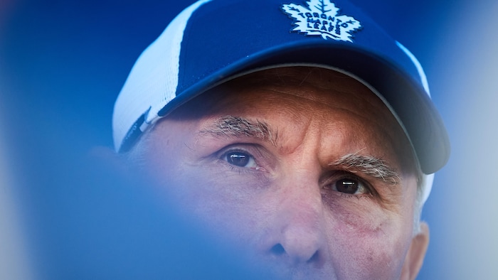 L'entraîneur regarde au loin. Il porte une casquette de l'équipe.