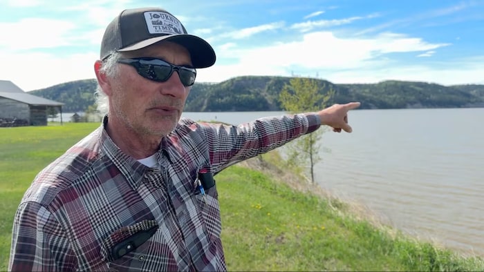 Un homme portant une casquette et des lunettes pointe son doigt vers une rivière.