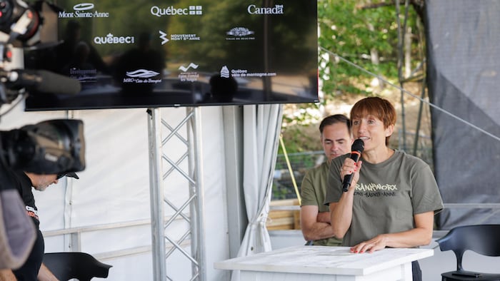 Debout derrière une table, elle parle au micro.