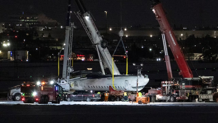 Un avion retourné est soulevé par deux grues pendant la nuit.