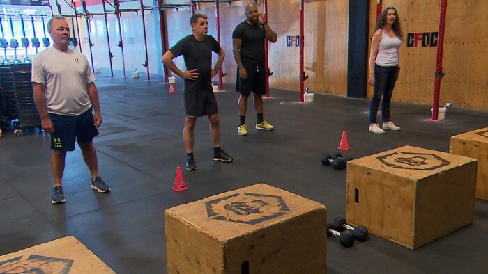 Quatre personnes debout dans un gym devant des blocs de bois pour l'entraînement.