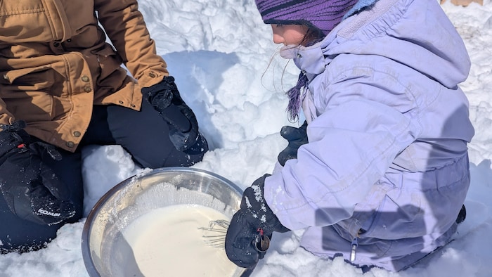 Une petite fouette la crème dans un bol métallique dans la neige.