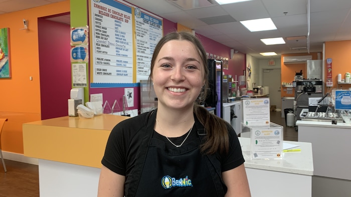 A teenage girl wearing a black apron faces the camera, back at the counter of a creamy, and smiles. not so easy find student not so easy find student new