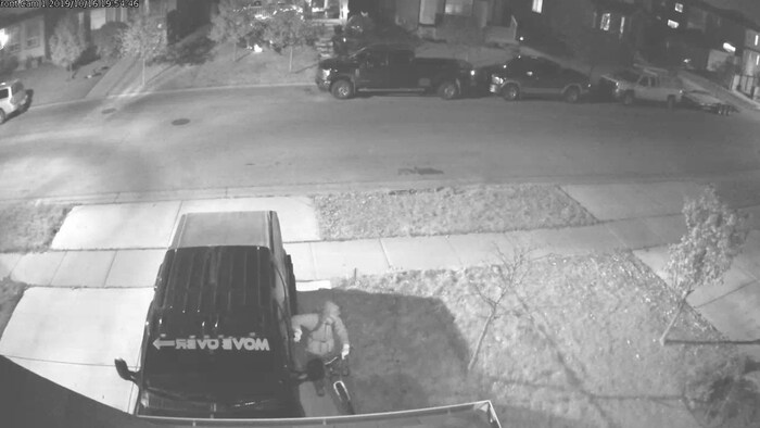 Une image en noir et blanc montre un homme en train d'essayer d'ouvrir la portière d'une voiture.