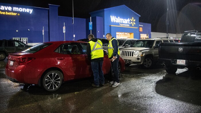 Deux hommes portant des dossards jaunes dans un stationnement d'un Walmart, le soir.
