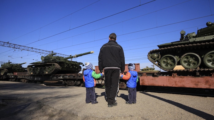Un homme et ses deux enfants observent l'arrivée de chars russes en Crimée.