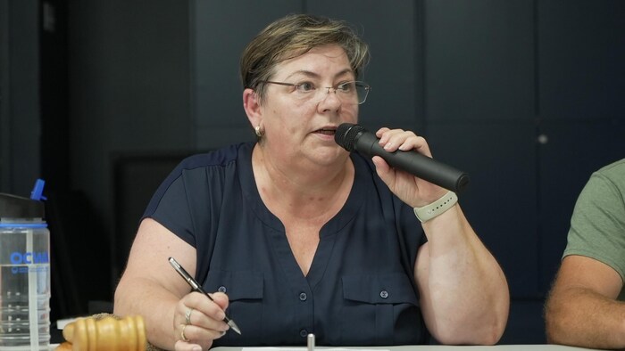 Madeleine Tremblay, assise à une table, parle aux gens dans un micro.  