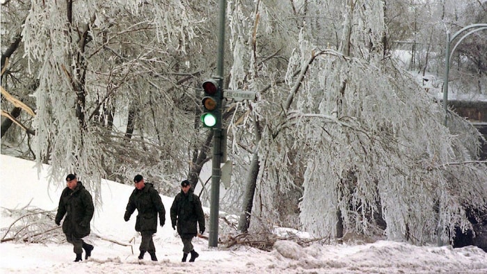 ثلاثة جنود يسيرون في شارع تنحني أغصان الأشجار فيه تحت ثقل الجليد.
