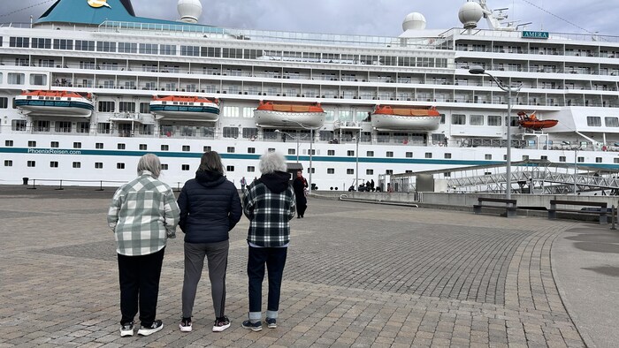 Trois femmes dont deux avec les cheveux blancs regardent un bateau. Elles sont photographiées de dos.