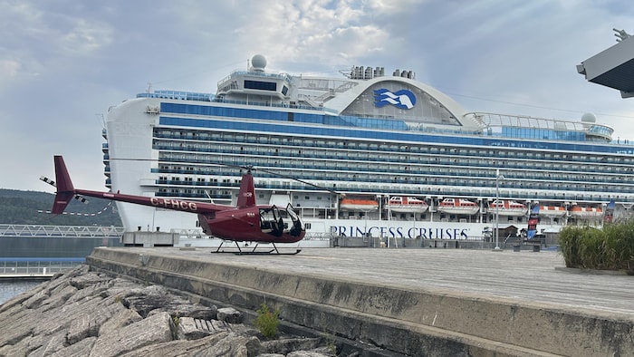Un hélicoptère est au sol devant un bateau.