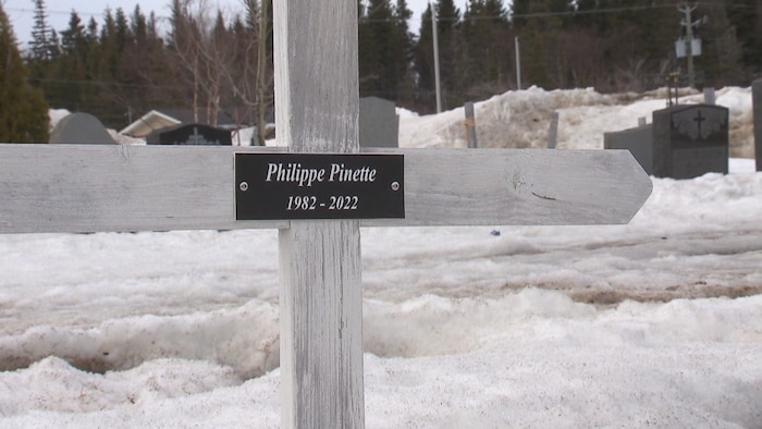 Une croix dans un cimetière enneigé sur laquelle on peut lire « Philippe Pinette 1982-2022 ».