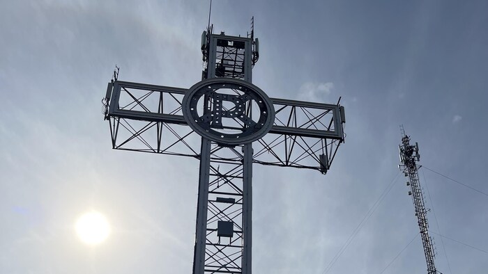 Vue en contre-plongée sur une croix de métal sur laquelle la lettre « P » est inscrite.