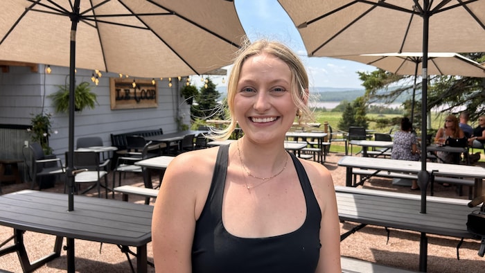 Une jeune femme souriante devant des tables de terrasse d'un établissement.