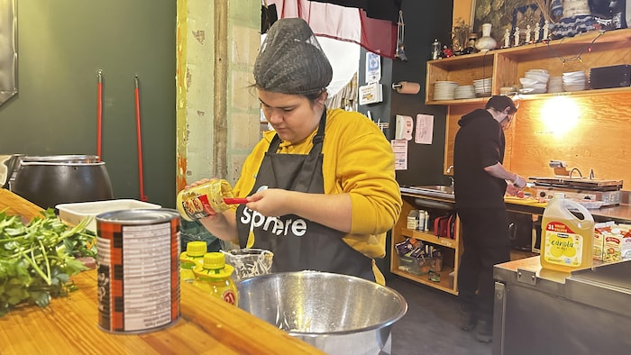 Une jeune femme dans la cuisine d'un restaurant verse de la moutarde de Dijon dans un saladier. 