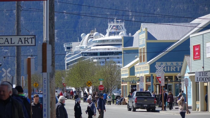Des touristes dans la rue principale de Skagway en été. Au loin, un bateau de croisière est amarré au port.